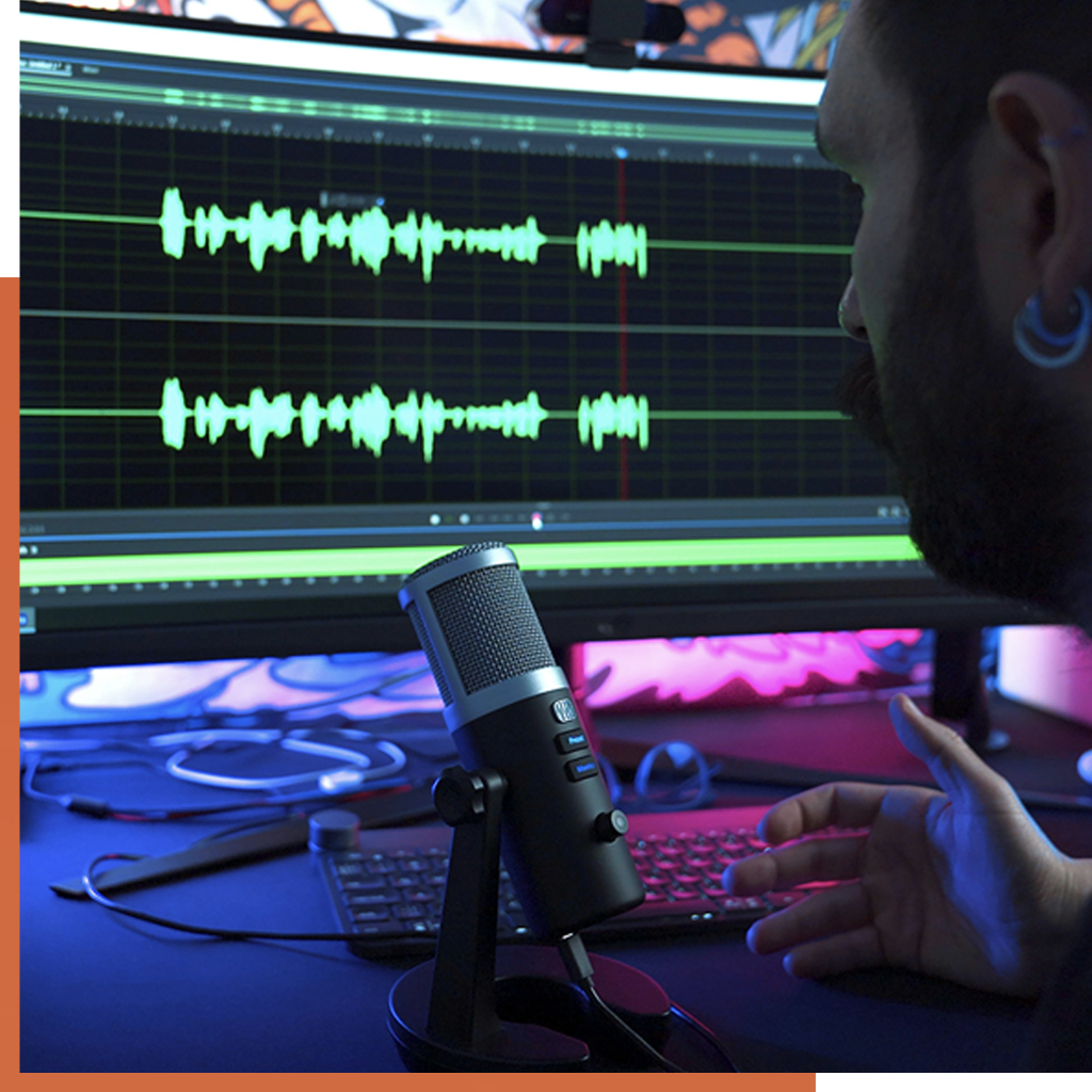 A person sitting at a desk with a microphone, editing audio on a computer screen displaying waveform patterns. Lighting creates a focused, tech-savvy ambiance.